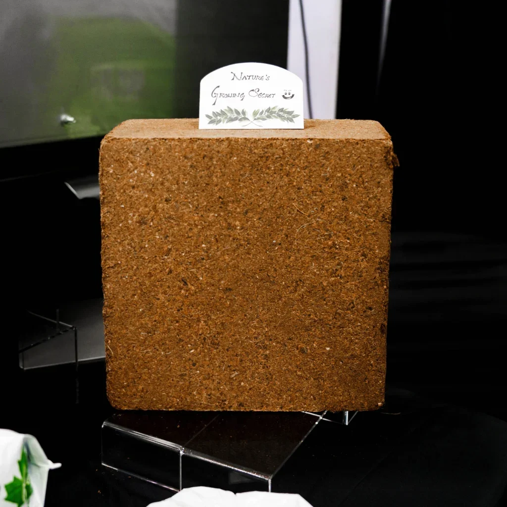 Premium compressed coco coir block by Avee Cocoseller on a display stand featuring a Nature's Growing Secret sign, ideal for greenhouse hydroponics.